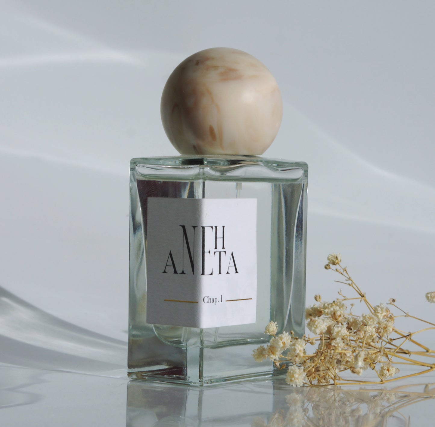 Le parfum Anehta vue de biais avec quelques fleurs séchées.
