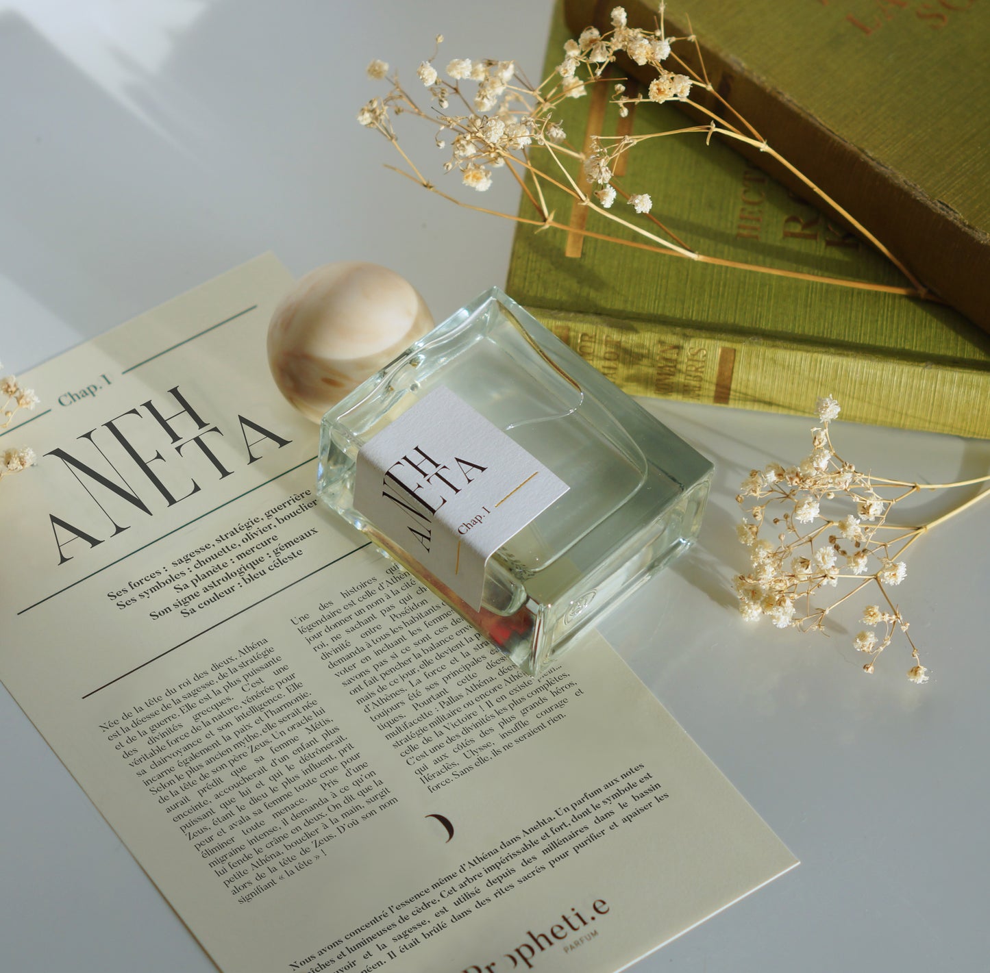 Parfum Anehta posé à plat sur le parchemin à plat, avec la pierre et quelques fleurs séchées ainsi que des livres