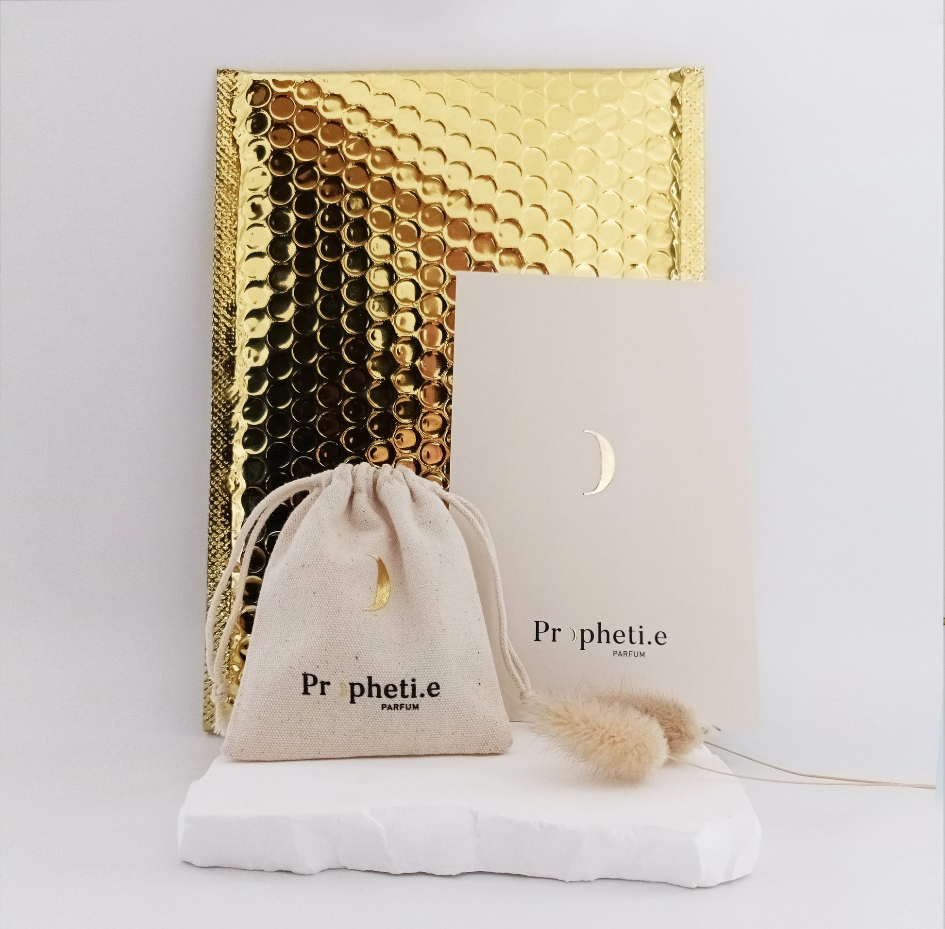 Un pochon Propheti.e, une pochette dorée, une carte Propheti.e debout sur une pierre ave une fleur séchée