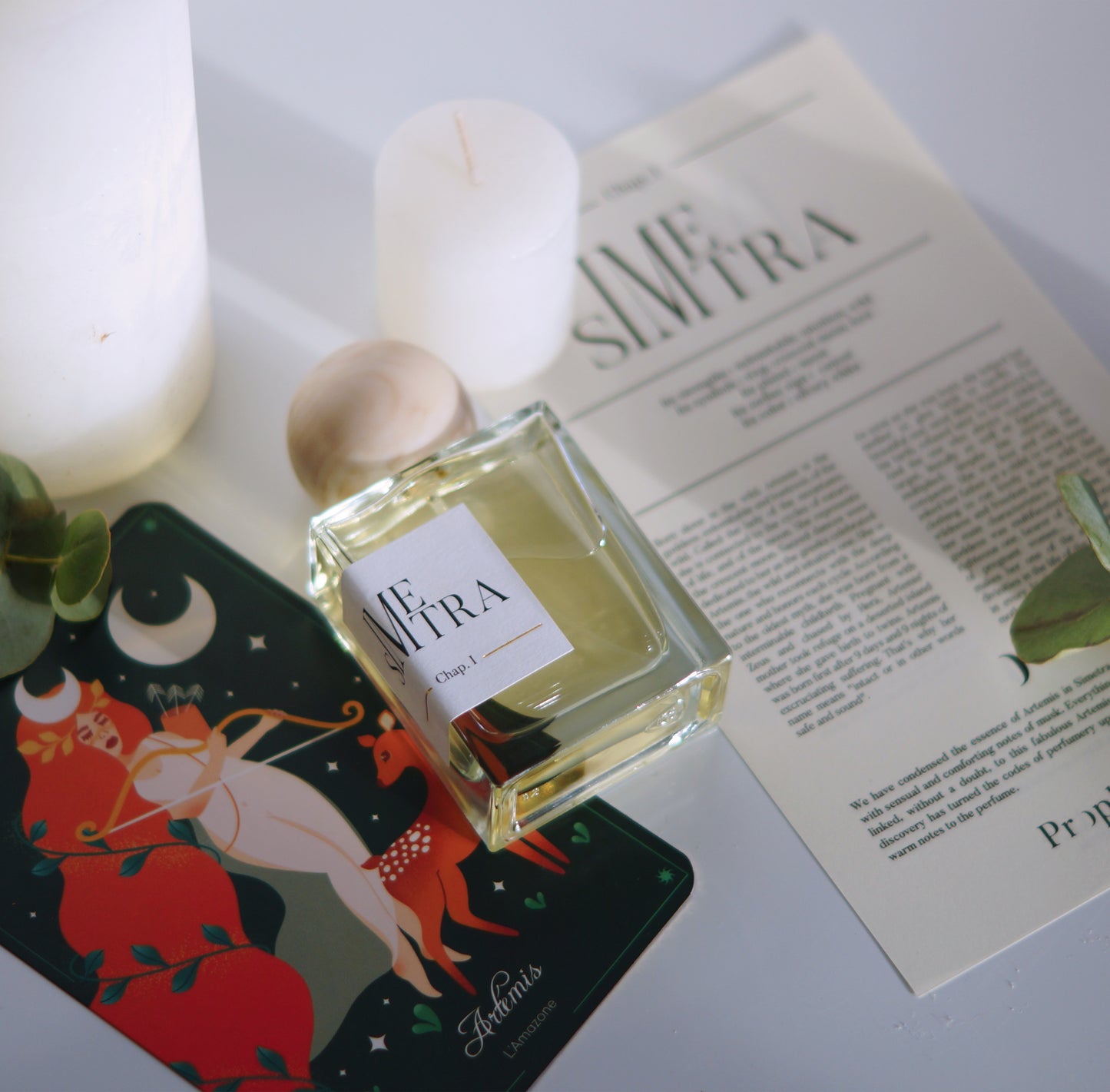 Parfum simetra posé à plat sur une carte Artémis avec le parchemin à plat et une bougie