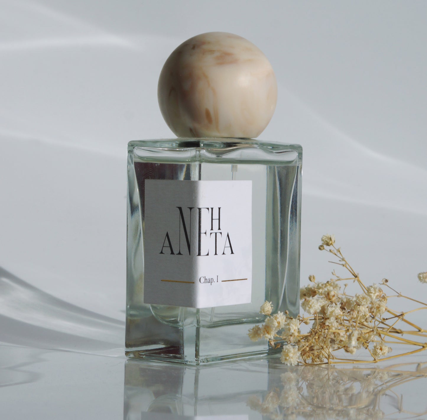 Le parfum Anehta vue de biais avec quelques fleurs séchées.