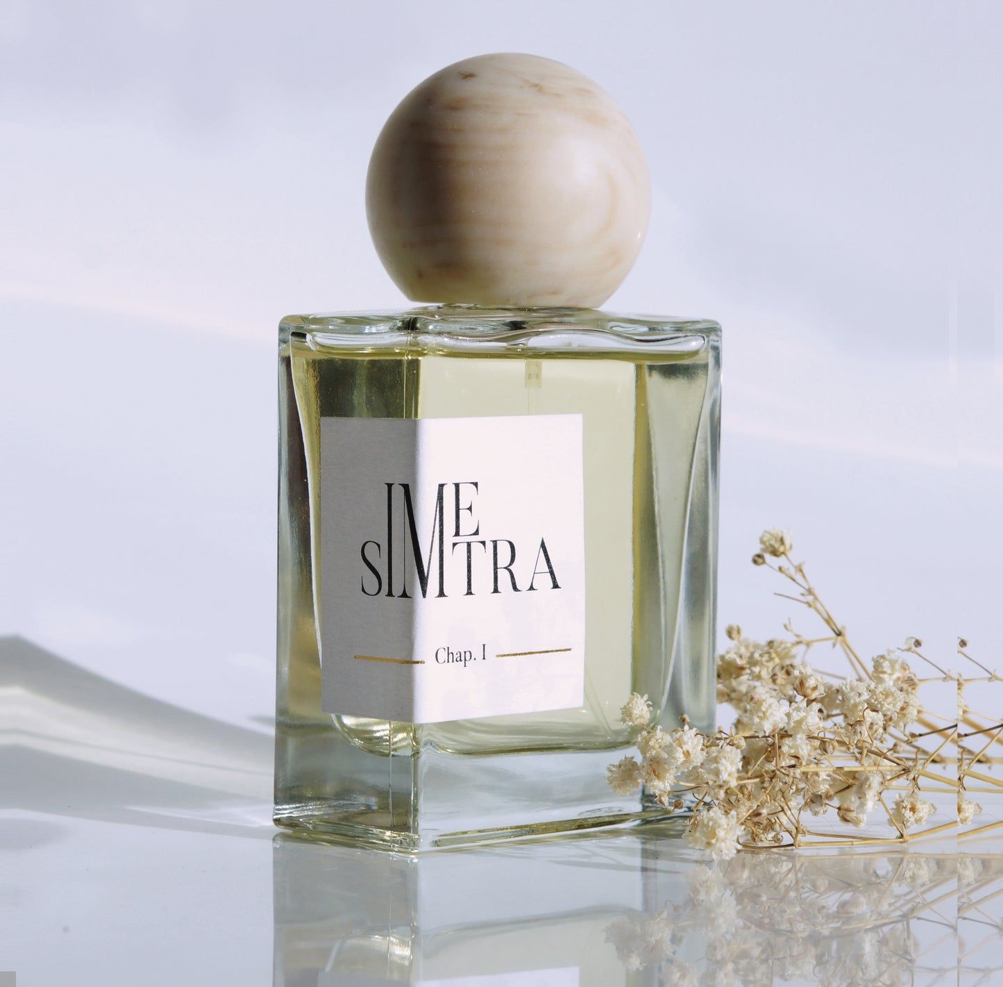 Le parfum Simetra vue de biais avec quelques fleurs séchées.